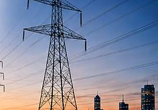 High-voltage transmission tower at dusk with a city skyline